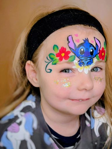 Mädchen mit Gesichtsbemalung von Stitch und bunten Blumenmotiven.