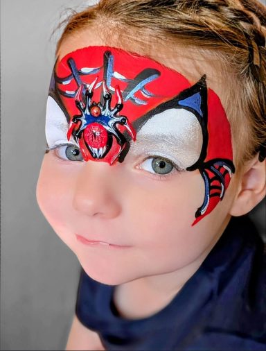 Ein Kind mit Spider-Man-Gesichtsbemalung auf der Stirn und neugierigem Blick.