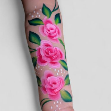 Bunter Arm mit tätowierten rosa Rosen und grünen Blättern.